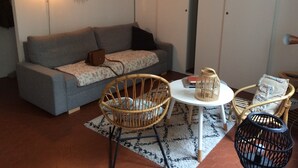 A cozy living room with a grey sofa, a wicker chair, a small round table, and a black floor lamp. - Studio Avec Jardin (Marseille)