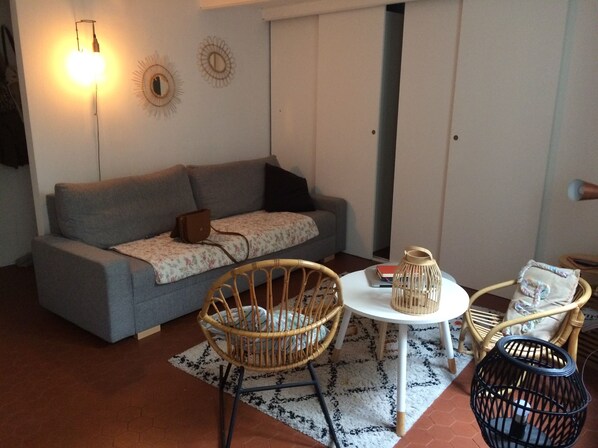 A cozy living room with a grey sofa, a wicker chair, a small round table, and a black floor lamp. - Studio Avec Jardin (Marseille)