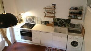 A compact kitchen with white cabinets, a stove, oven, sink, and a washing machine. - Studio Avec Jardin (Marseille)