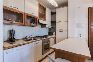 Une cuisine compacte équipée d’un lave-vaisselle, d’une cuisinière, d’un four à micro-ondes et de meubles de rangement en bois.