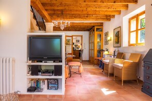 A cozy living room with a television, bookshelves, wicker furniture, and a wooden ceiling. - Country Home Son Pi with Mountain View, Pool, Wi-Fi, A/C, Terrace & Garden (Llorenc del Cardassar)