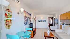 A living room with a TV, a dining area with chairs, a sofa, and a kitchen area with cabinets. - Apartment Vista Mar 4ºE on the Beach with Sea View, A/C & Balcony (Armação de Pêra)