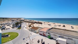 A coastal road with a beach, parked vehicles, and a building with a sign. - Apartment Vista Mar 4ºE on the Beach with Sea View, A/C & Balcony (Armação de Pêra)