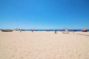 Une plage avec du sable, des bateaux et des parasols.