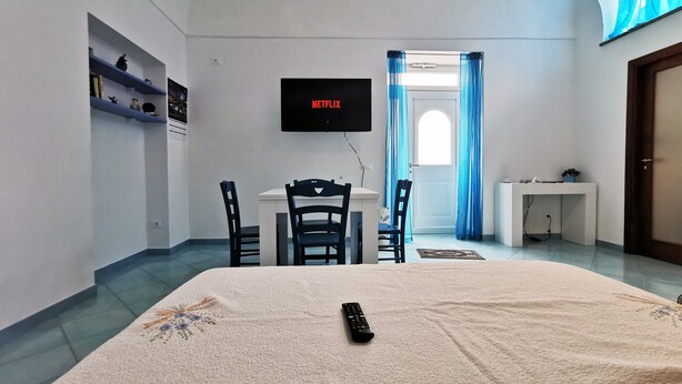 Ein Zimmer mit einem Bett, einem Schreibtisch, einem Sessel, einem an der Wand befestigten Fernseher und einem Fenster mit Vorhängen.