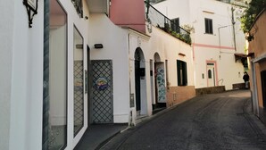 Eine enge Straße mit Häusern an beiden Seiten, einem blauen Hinweisschild und einer Tür mit einem Metallgitter.