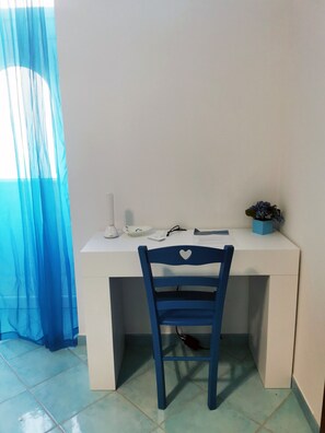 Un bureau blanc, une chaise bleue, une plante en pot et une fenêtre avec des rideaux bleus.