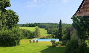 A rustic building with a tiled roof, surrounded by lush greenery and a clear blue sky.
