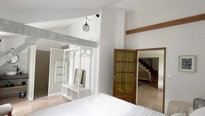 Een slaapkamer met een groot bed, een inloopkast, een badkamer met een wastafel en een trap die naar een andere verdieping leidt.