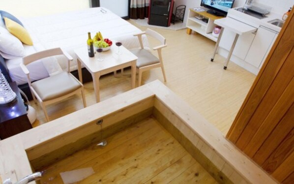 A room with a wooden hot tub, a dining area with a table and chairs, a kitchen area, and a bed with pillows. - Wonju Cloud Pension (Wonju)