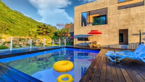 Ein moderner Poolbereich mit Holzterrasse, Liegestühlen und einem roten Sonnenschirm.