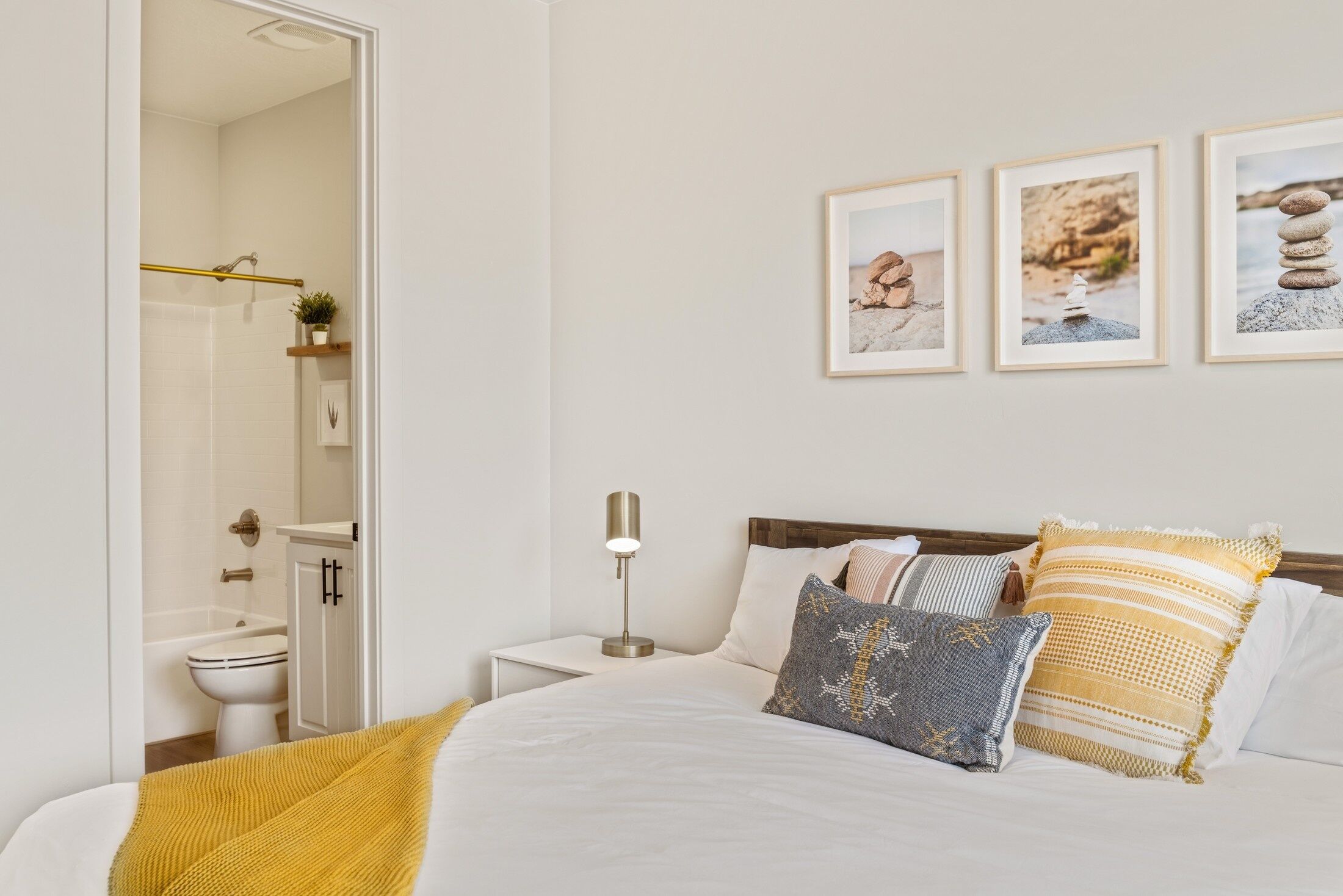 A bedroom with a bed, bedside table, lamp, and framed pictures on the wall.