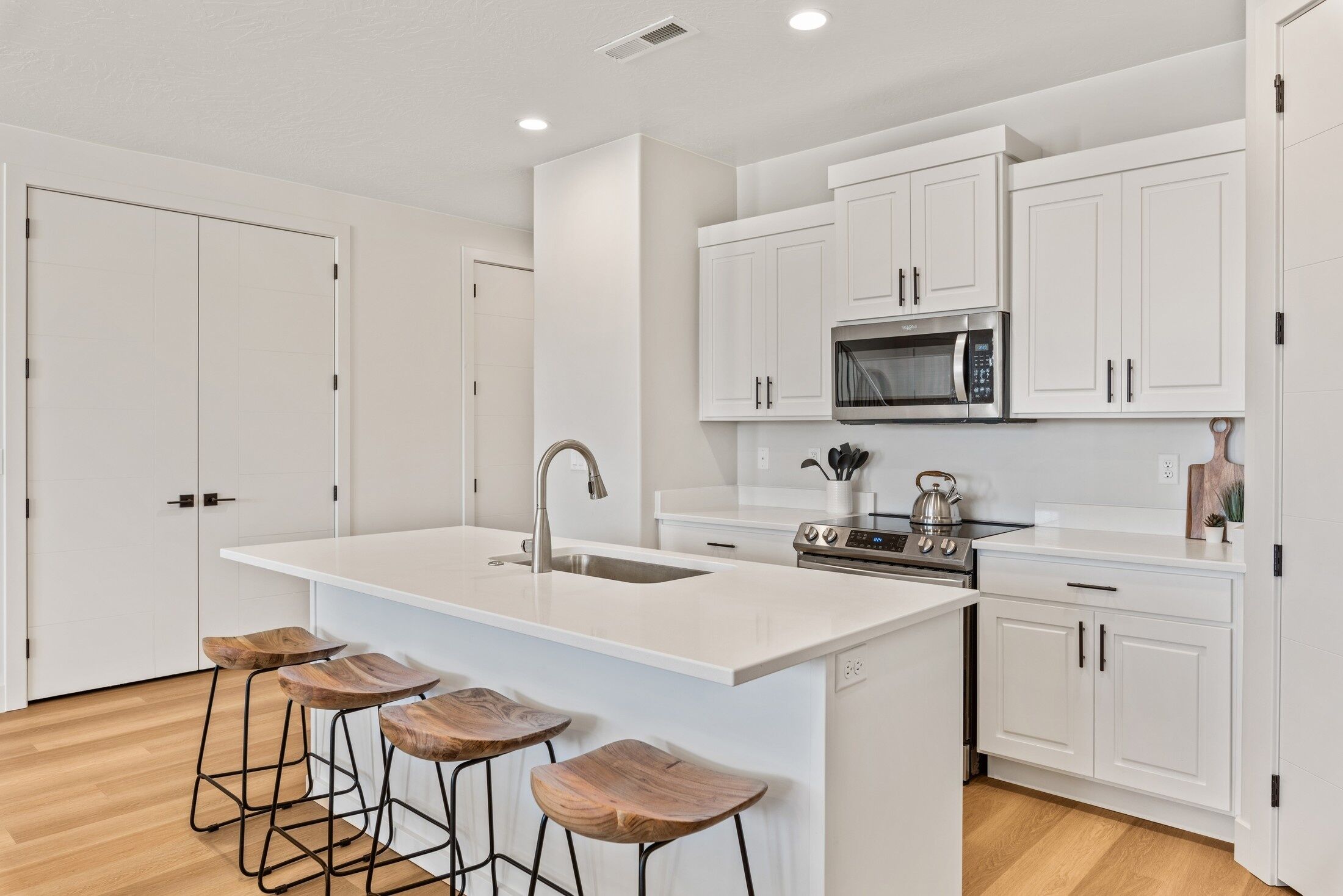 A modern kitchen with white cabinetry, a large island with stools, a stainless steel sink, and a built-in microwave.