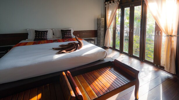 A large bed with a wooden headboard, a bench at the foot of the bed, and a view of greenery through the window. - Stay in resedential house in pasig city (Pasig)