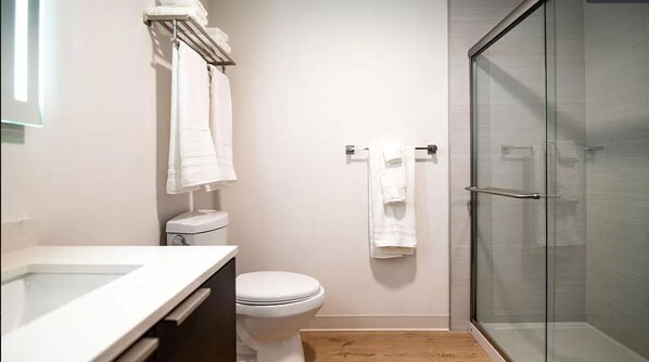 A modern bathroom with a glass shower enclosure, a white toilet, and a sink with a towel rack above it.