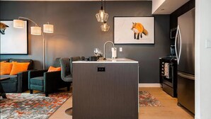 Eine moderne Küche mit einer zentralen Kochinsel, einem Essbereich mit einer Couch und Sesseln sowie einem Kühlschrank.