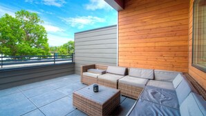 Ein Balkon mit Korbmöbeln, gefliestem Boden und Blick auf Bäume und eine Straße.
