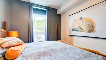 A bedroom with a bed, a window with curtains, a table and chairs outside, and a framed picture on the wall.
