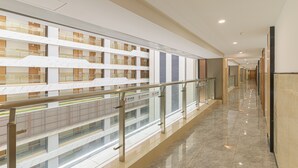 A modern hotel corridor with a glass railing, a clean tiled floor, and multiple floors visible through the glass. - Bainianhui International Apartment (Foshan)