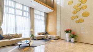 A modern living room with a beige sofa, a coffee table, and a large window with sheer curtains. - Bainianhui International Apartment (Foshan)