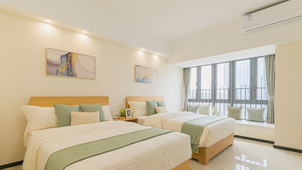 A hotel room with two beds, large windows, and artwork on the walls. - Bainianhui International Apartment (Foshan)