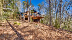 Une cabane en bois dotée d’une terrasse et de grandes fenêtres, entourée d’arbres.