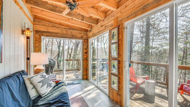 L’intérieur d’un chalet en bois, avec une grande porte vitrée donnant sur une terrasse, un canapé bleu et un ventilateur de plafond.