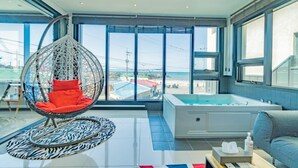 A modern room with a hanging chair, a bathtub, and a view of the sea. - Jeju Judith Pension (Jeju City)