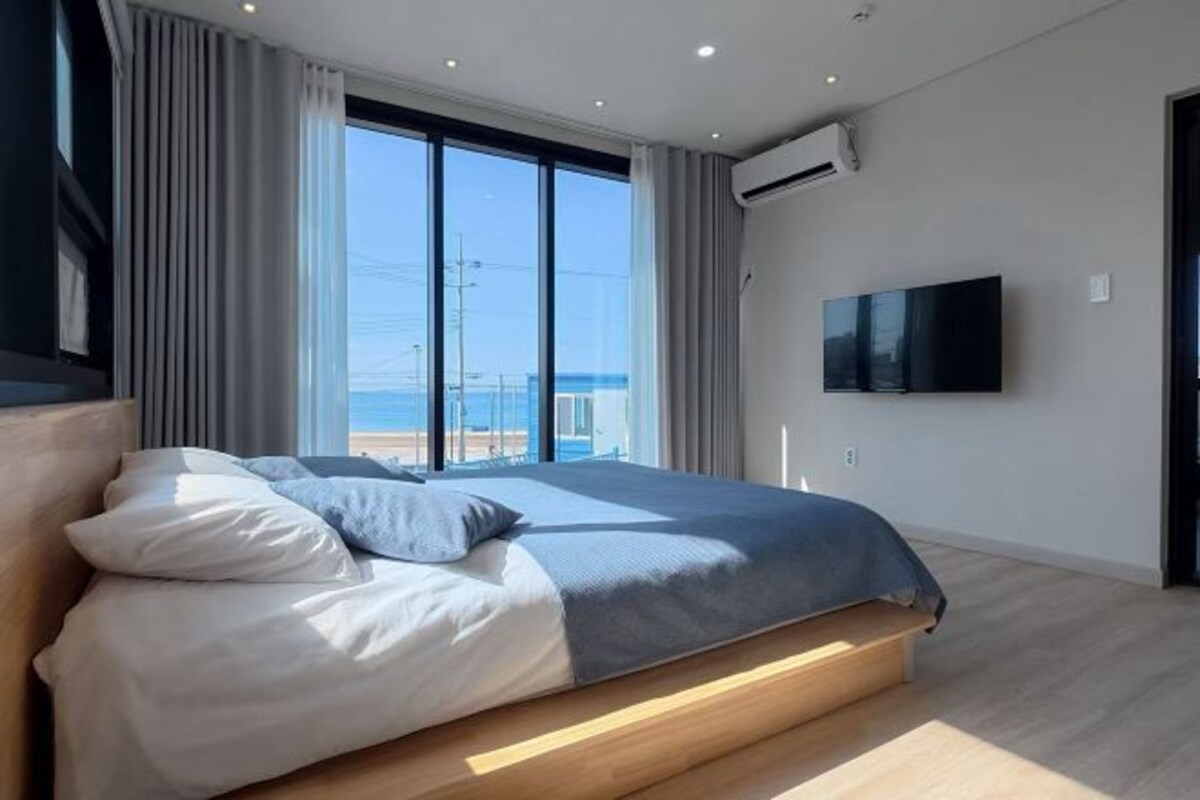 Quarto moderno com uma cama grande, televisão na parede e vista para o mar.