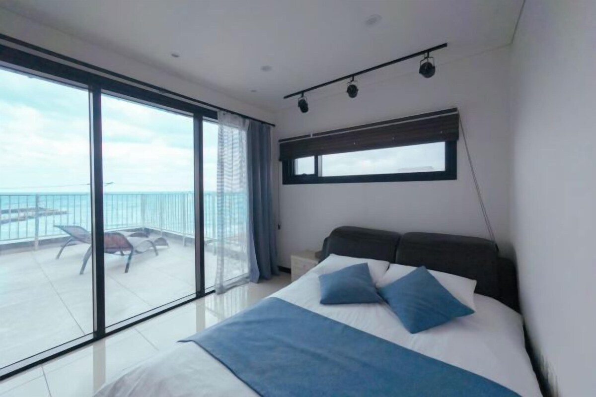 Um quarto moderno com uma cama grande, uma varanda com vista para o mar e uma janela com persianas.