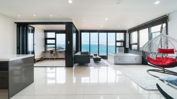 A spacious living area with a view of the sea, a modern kitchen, and a seating area with a hanging chair. - Jeju Judith Pension (Jeju City)
