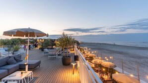 A deck with outdoor seating, a large umbrella, and a view of the beach. - Club Del Sole Pini Boutique Resort (Ravenna)