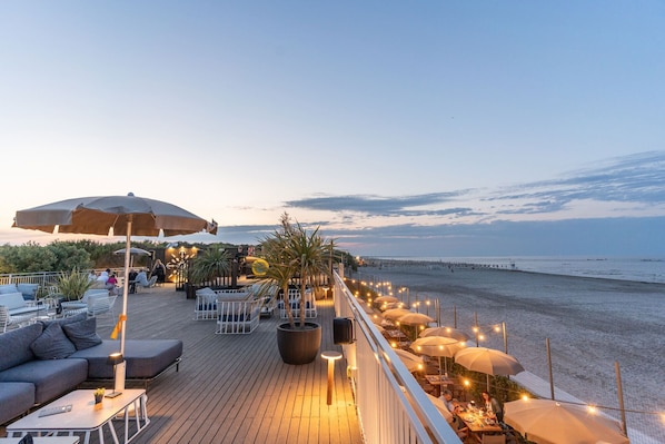 A deck with outdoor seating, a large umbrella, and a view of the beach.