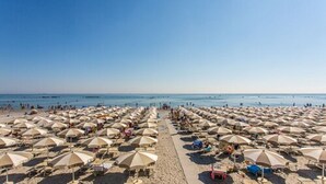 A beach with rows of umbrellas and beach chairs, a clear sky, and the ocean in the background. - Club Del Sole Pini Boutique Resort (Ravenna)