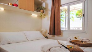 A hotel room with a bed, a window with curtains, a shelf with decorative items, and a view of greenery outside. - Club Del Sole Pini Boutique Resort (Ravenna)