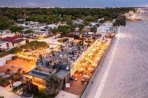 A coastal hotel with outdoor seating areas, a beach view, and a row of cabins.