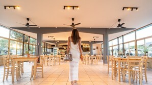 A spacious indoor area with multiple wooden tables and chairs, ceiling fans, and large windows allowing natural light. - Club Del Sole Pini Boutique Resort (Ravenna)