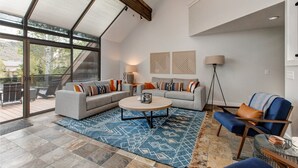 A modern living room with a large glass door leading to an outdoor deck, a round coffee table, and a blue patterned rug. - Step into Your Luxury Condo Today - Hot Tub & Wi-Fi Access! (Park City)