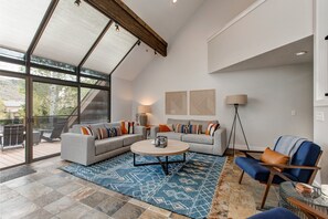 A modern living room with a large glass door leading to an outdoor deck, a round coffee table, and a blue patterned rug.