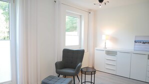 A modern room with a grey upholstered chair, a matching ottoman, a small round table, and a white cabinet with drawers. - Fewo Wagner +nur 10 Gehminuten bis zum Ostseestrand+ - Ferienwohnung Wagner (Koserow)