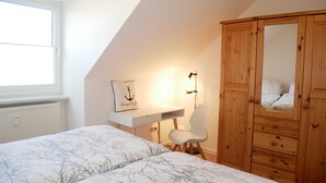 A bedroom with a sloped ceiling, a bed with a tree-patterned duvet, a wooden wardrobe, a white desk with a lamp, and a window. - Fewo Wagner +nur 10 Gehminuten bis zum Ostseestrand+ - Ferienwohnung Wagner (Koserow)