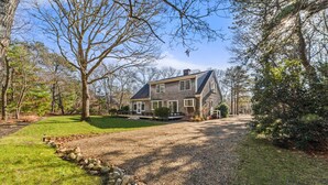 A two-story house with a stone foundation, a large front lawn, and a driveway leading to the entrance. - Family Fun, Spacious+Game Room (Oak Bluffs)