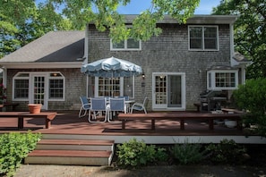 Une maison à deux étages dotée d’un patio, d’un espace salon extérieur et d’un barbecue.