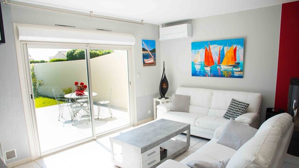 A modern living room with a white sofa, a coffee table, and a glass door leading to a patio with outdoor furniture. - HOUSE, CONTEMPORARY COMFORT AND TRANQUILITY 15 MINUTES FROM THE BEACH  (Mauguio)