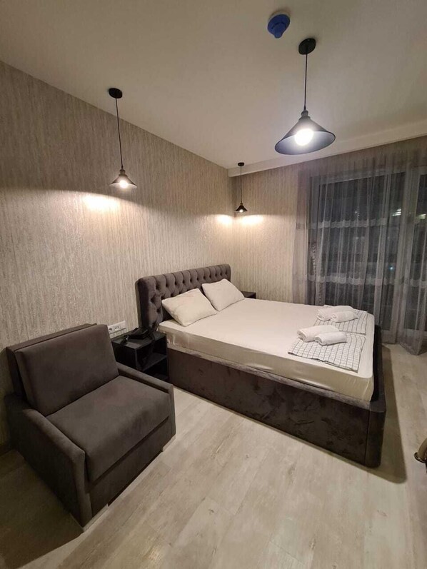 A modern bedroom with a large bed, a chair, and two pendant lights.