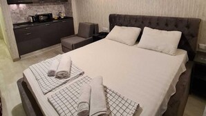 Un dormitorio moderno con una cama grande, una zona de estar separada, una kitchenette y una lámpara colgante.