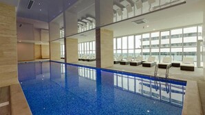 Una piscina interior moderna con paredes de vidrio transparente, sillones de descanso y vistas a la ciudad.