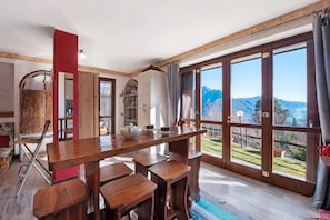Cocina amplia con una gran mesa de madera y sillas, vistas a montañas a través de ventanas grandes y una pared de acento roja.