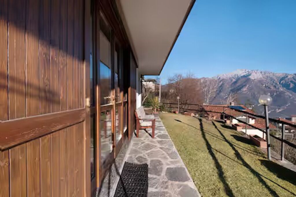 Un bâtiment en bois avec une terrasse en pierre, une chaise et une vue sur les montagnes.