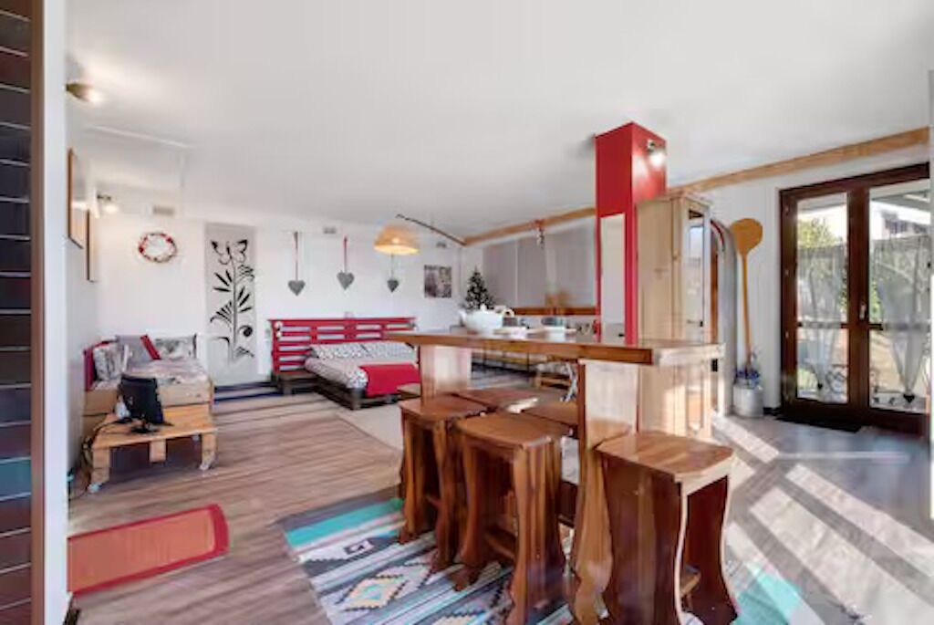 Una sala de estar moderna con un sofá, taburetes de madera, una mesa de comedor y una cocina.